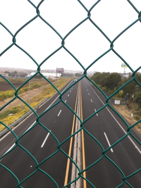 Foto estrada vista através de uma cerca de cadeia contra um céu claro