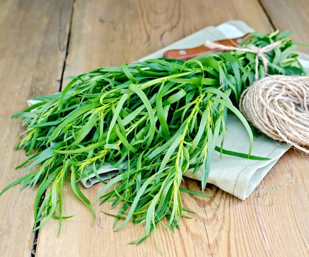 Estragão verde fresco com uma bola de barbante e uma faca em um guardanapo no fundo de tábuas de madeira