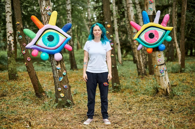 Estranha jovem adulta com cabelo turquesa tingido em camiseta branca perto de instalação de arte de olhos grandes