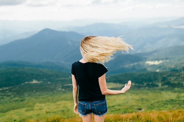 Estranha jovem incomum estranha brincando com o cabelo nas montanhas. De trás retrato humor de cabelos longos loiro bebê ao ar livre. Estado de espirito. Alpinista feminina relaxante na natureza. Bela paisagem