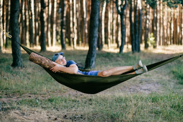 Estranho estranho homem do sexo masculino incomum. estranho engraçado louco homem tolo dormindo na rede com enorme tronco de madeira na natureza entre árvores. com viga na cama.