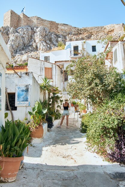 Estrecha calle griega con muchas plantas y casas en la montaña y una chica con sombrero pasión por