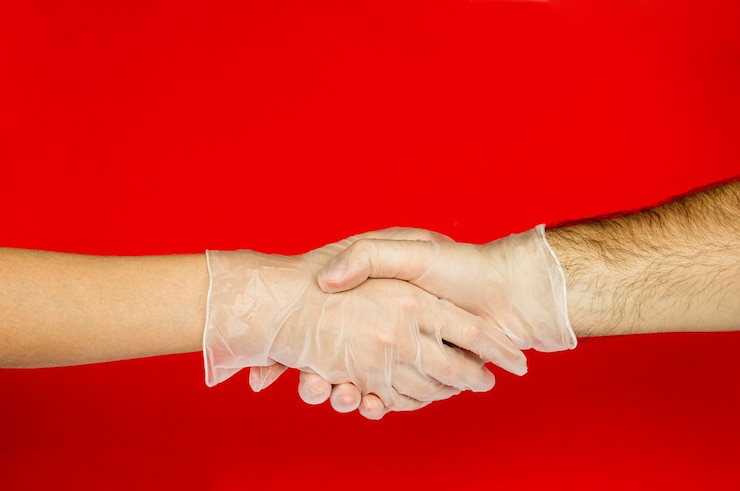 Estrechar la mano de hombres y mujeres en guantes médicos sobre fondo rojo. COVID-19.Coronavirus. Protección contra el virus.