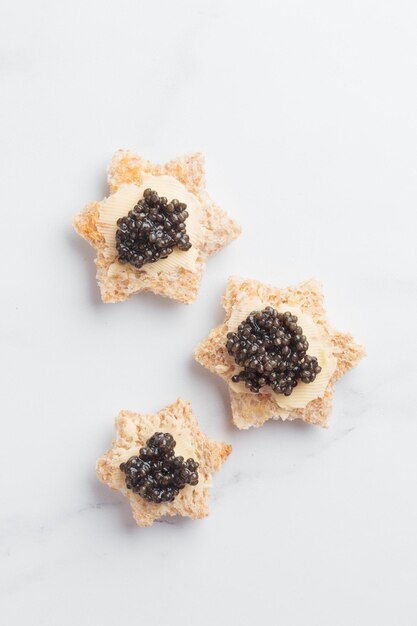 Estrela de pão de aperitivos de caviar preto em uma vista superior de fundo branco