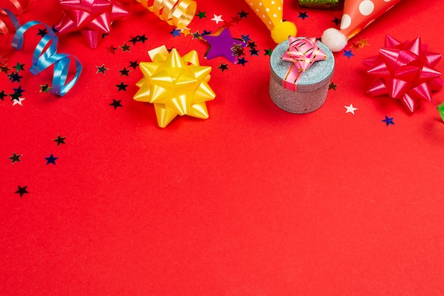 Estrelas festivas douradas e roxas de confete e um presente, bonés de aniversário em um fundo vermelho. Espaço para texto ou desenho.