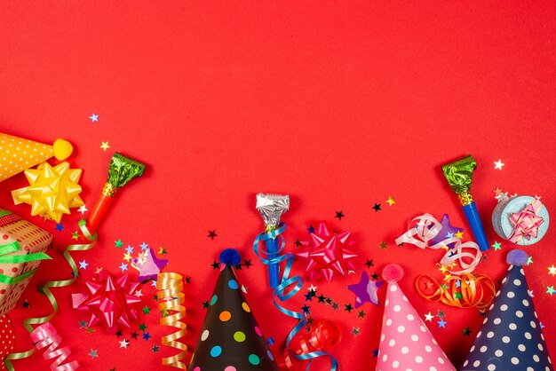 Estrelas festivas douradas e roxas de confete e um presente, bonés de aniversário em uma superfície vermelha.