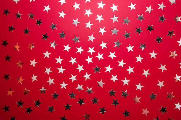 La estrella de plata asperja en backgound rojo. Confeti festivo de vacaciones. Concepto de celebración