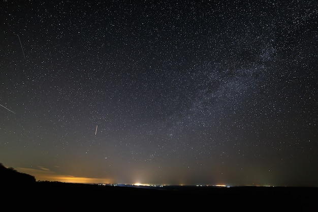 Estrellas en el cielo de la noche oscura con luces de la ciudad en el horizonte.