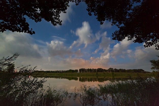 Estrellas en el cielo con nubes. Paisaje nocturno con un lago.