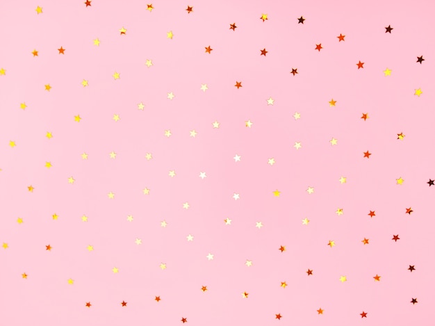 Foto las estrellas doradas brillan sobre un fondo de moda de tonos pastel rosa. confeti cayendo. fondo festivo para tus proyectos.