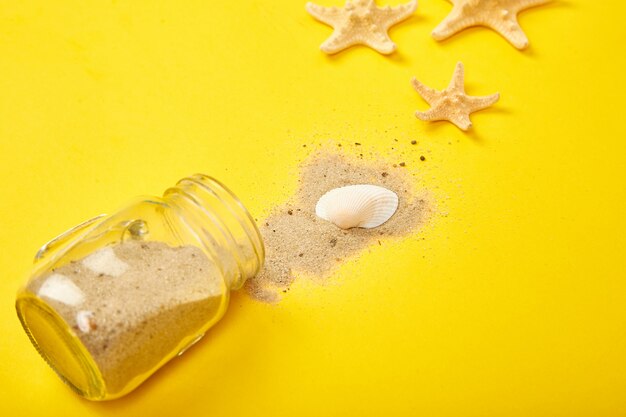 Estrellas de mar y conchas marinas, vidrio con arena sobre fondo amarillo