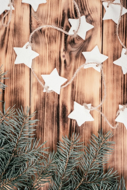 Estrellas de Navidad guirnalda de porcelana fría casera con ramas de abeto sobre fondo de madera quemada, vista superior. Vertical