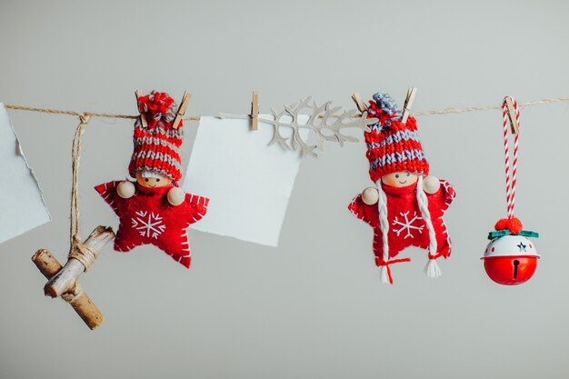 Estrellas de Navidad de punto rojo con sombreros divertidos. Muñecos de Navidad y adornos colgando de la cuerda con pinza para la ropa. Trozo de papel blanco para texto.