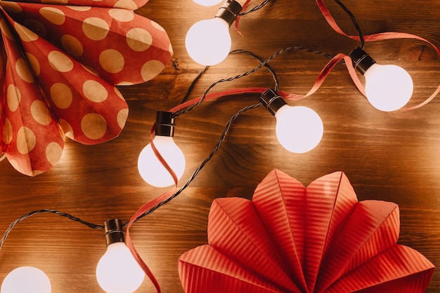 Estrellas de papel nórdicas con guirnaldas de luces led blancas y hilo rojo sobre mesa de madera navidad sostenible...