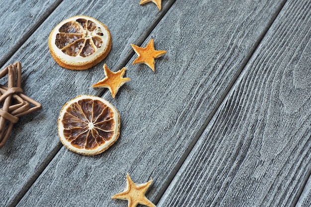 Estrellas secas hechas de cáscara de naranja y rodajas de naranja secas redondas y estrella de mimbre sobre fondo gris madera.