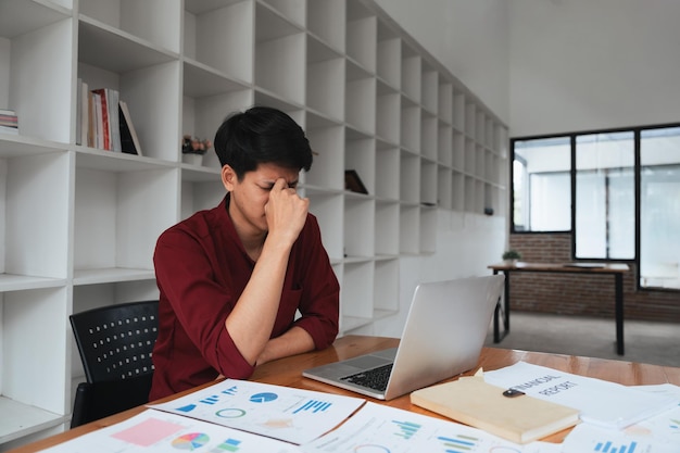 Foto estrés, ansiedad y agotamiento con el trabajo, un hombre de negocios en el trabajo usando una computadora portátil mientras sufre dolor de cabeza