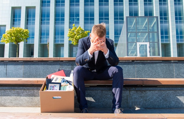 Foto estrés y concepto de desempleo, ex empleado sentado con sus pertenencias metidas en una caja a su lado