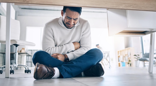 Estrés empresarial, llanto y agotamiento de un empleado de la oficina que sufre de problemas de salud mental Hombre de negocios de la empresa con dolor de estómago y sentimiento de tristeza bajo el escritorio corporativo con depresión del trabajo