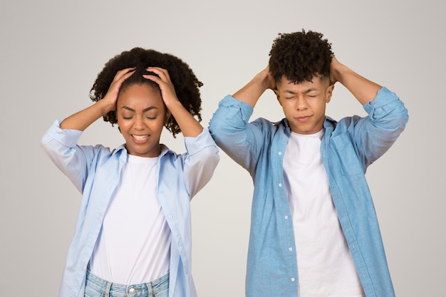 Estresada joven afroamericana y hombre con las manos sobre la cabeza los ojos cerrados