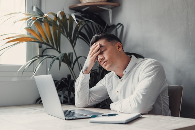 Estresado hombre cansado en el dolor teniendo un fuerte ataque de dolor de cabeza terrible después de la computadora portátil