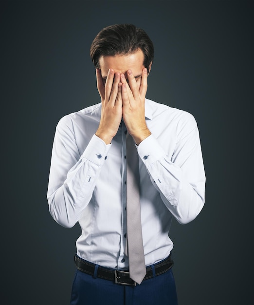 Estresar y encontrar el concepto de solución con el hombre de camisa blanca cerrando los ojos con la palma de la mano aislado en el fondo gris oscuro