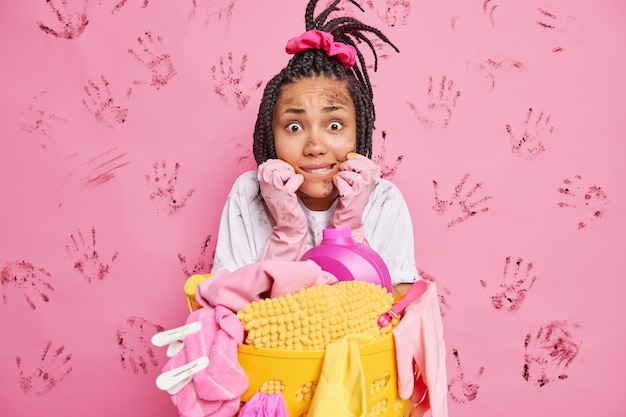 Estressada e nervosa, jovem afro-americana tem o rosto sujo e morde os lábios na parede rosa com marcas de mãos