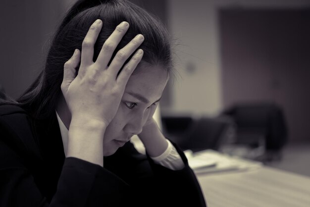 Estresse de empresária asiática por trabalho duroMulher trabalhadora tailandesa trabalhando no escritórioTom escuro
