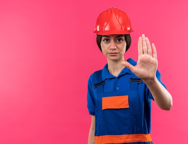 Estricto mirando a cámara joven constructor mujer en uniforme mostrando gesto de parada