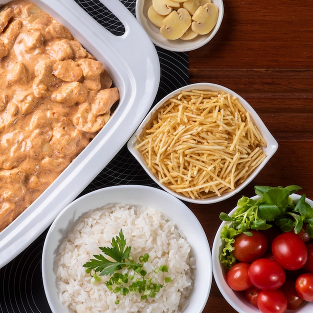 Estrogonofe de frango acompanhado de arroz, salada e palha de batata.