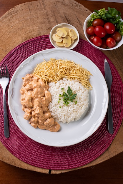 Estrogonofe de frango acompanhado de arroz, salada e palha de batata.