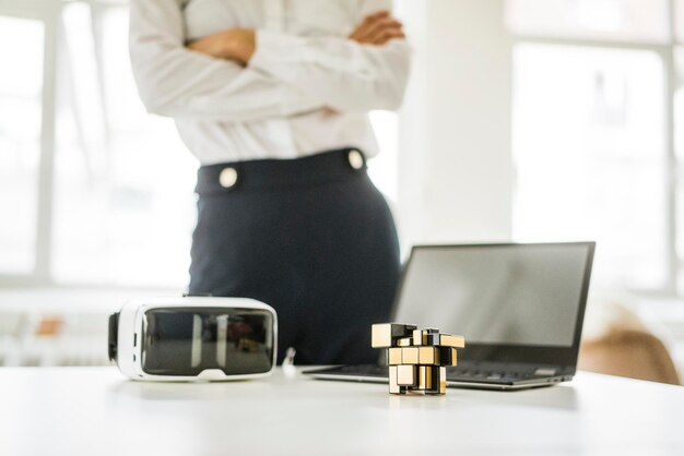 Estructura cúbica, gafas VR y computadora portátil en el escritorio de la oficina con una mujer de negocios en segundo plano.