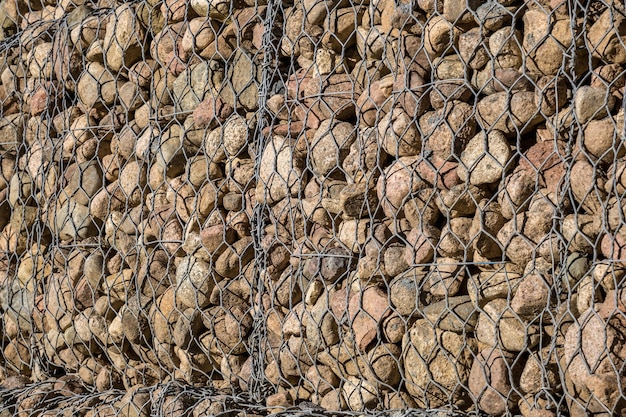 Estructura de ingeniería hecha de piedras detrás de una tela metálica para fortalecer la orilla del río cerca del puente de la carretera