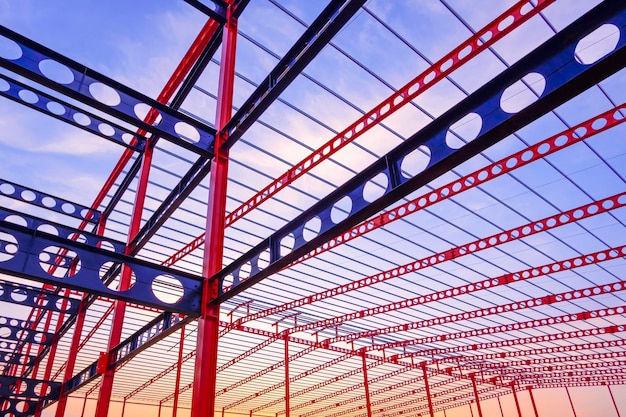 Estructura de viga almenada de metal rojo y azul de un gran edificio industrial contra el cielo del atardecer