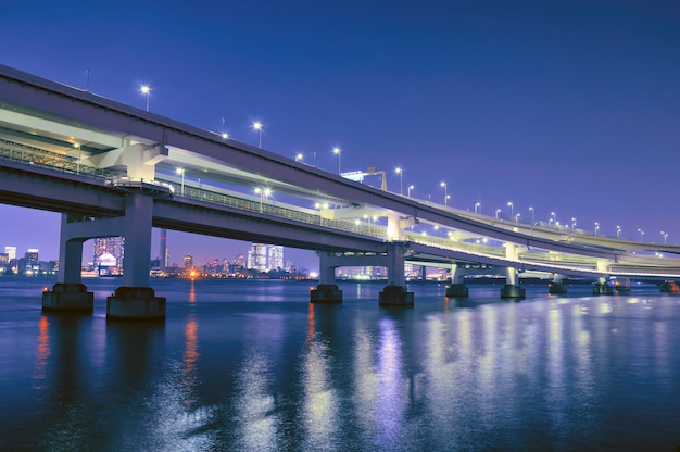 Estrutura da ponte sobre as águas da baía noturna com iluminação panorâmica em tóquio, japão