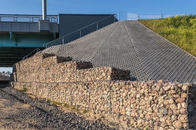 Estrutura de engenharia feita de pedras atrás de rede metálica para fortalecer a margem do rio perto da ponte rodoviária