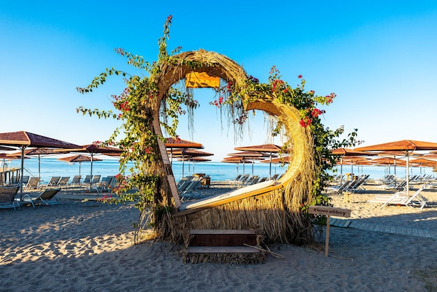 Estrutura em forma de coração decorada com plantas e flores exibidas na praia com mar e céu azul claro