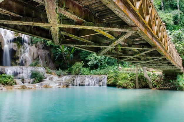 Estrutura velha da ponte de aço sobre o rio e o fundo da cachoeira em kuang si waterfalls