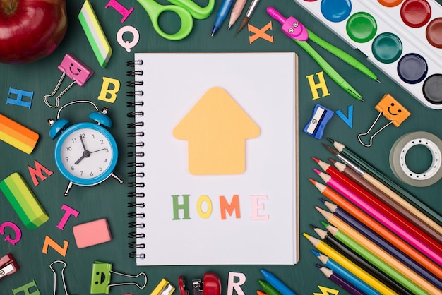 Foto estudando no conceito de casa. foto de cima acima de vista aérea de um caderno em branco com letras iniciais e nota em forma de casa e papel de carta colorido isolado no quadro verde