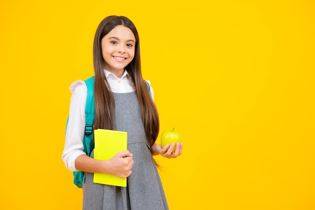 Estudante adolescente adolescente com mochila segura maçã e livro isolado em amarelo