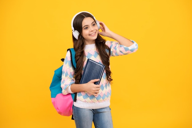 Estudante adolescente colegial em fones de ouvido segura livros sobre fundo amarelo isolado do estúdio Escola