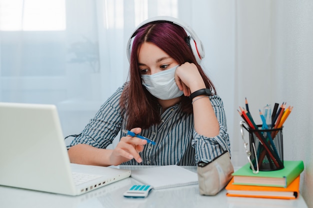 Estudante adolescente com máscara médica contra vírus sentado chão estudante sala sofá estudando em casa laptop fazendo lição de casa