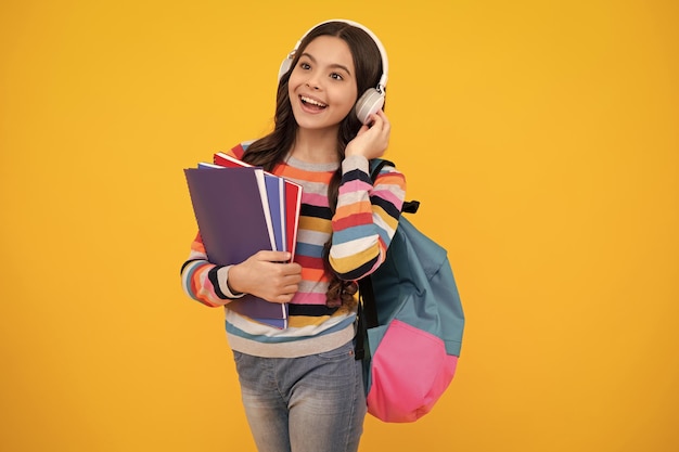 Estudante adolescente da escola em fones de ouvido segura livros sobre fundo amarelo isolado do estúdio Conceito de educação escolar e musical Adolescente feliz emoções positivas e sorridentes de adolescente