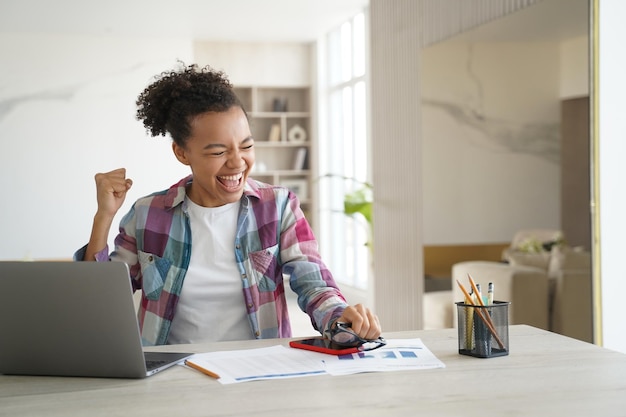 Estudante adolescente de raça mista animada recebeu um e-mail de boas notícias no laptop comemora conquista pessoal