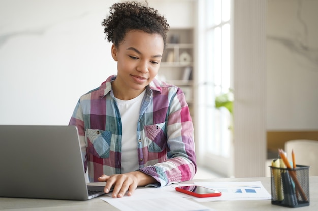 Estudante adolescente de raça mista aprendendo no laptop olha no celular ler mensagem na rede social