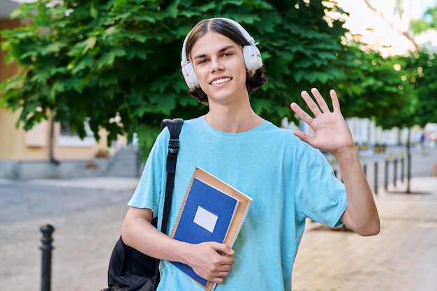 Estudante adolescente do sexo masculino sorridente com livros didáticos olhando para a câmera ao ar livre