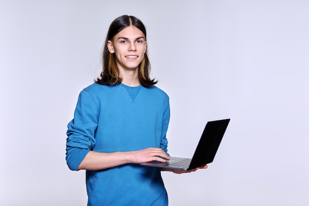 Estudante adolescente do sexo masculino usando laptop posando olhando para a câmera no fundo claro do estúdio