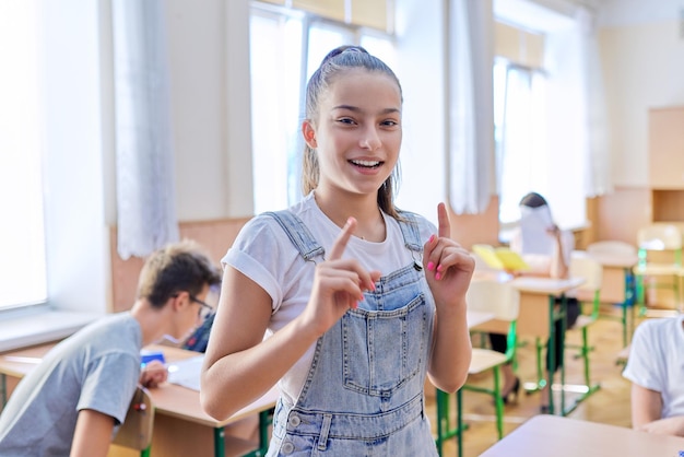 Estudante adolescente responde lição, falando olhando para a câmera, sala de aula com fundo de estudantes de estudo. Escola, educação, conceito de juventude