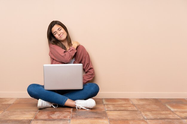 Estudante adolescente sentado no chão com um laptop sofrendo de dor no ombro por ter feito um esforço