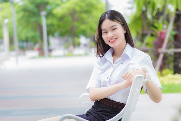 Estudante adulto tailandês com uniforme de estudante universitária menina asiática linda sentada sorrindo alegremente