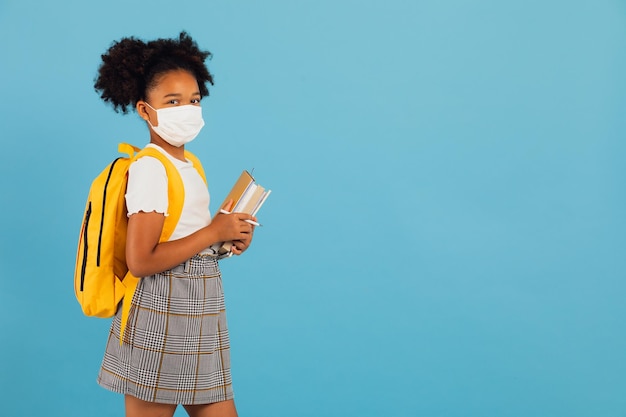 Estudante afro-americana em máscara segurando livros em fundo azul com espaço de cópia De volta ao conceito de escola COVID19